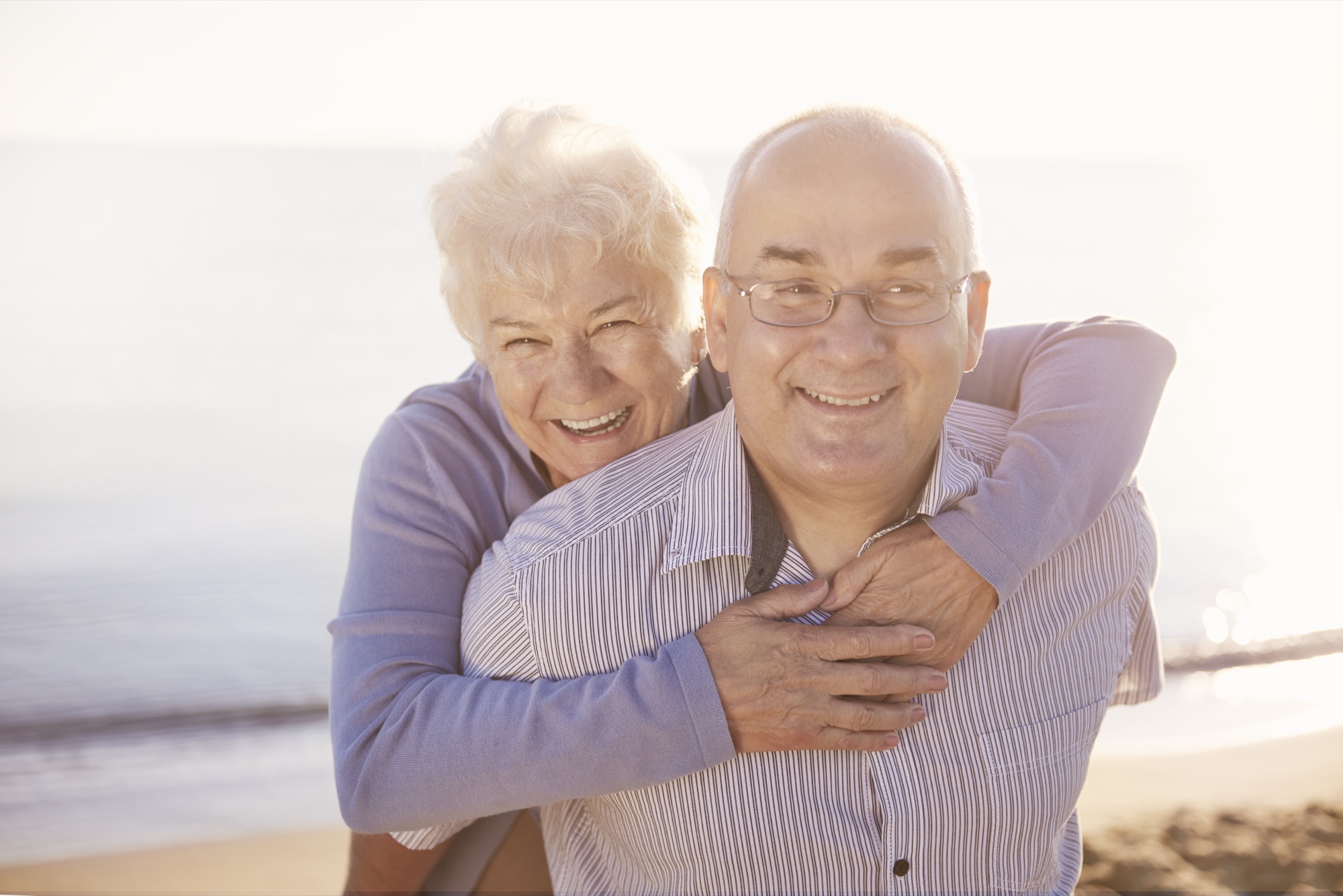 Happy senior couple enjoying a sunny Florida beach after successful cataract surgery at Filutowski Eye Institute